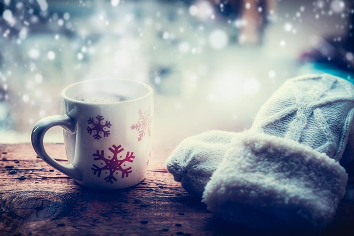 A cup of cocoa and gloves sitting in front of a snowfall